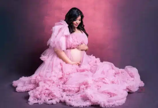 Pregnant woman in a flowing pink gown posing gracefully during a maternity photoshoot.