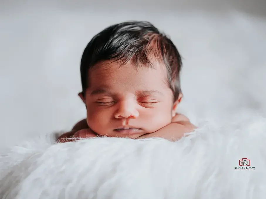 Newborn baby with chin resting on hands, peacefully sleeping on a fluffy white blanket