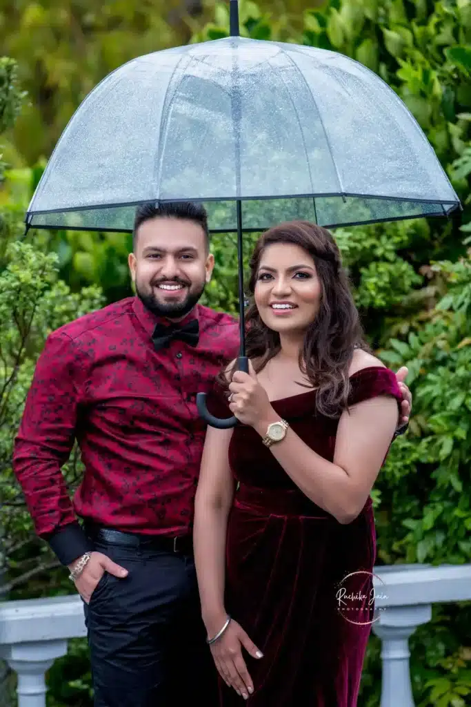 Romantic Rainy Photoshoot: A couple dressed in red shares a tender moment, holding an umbrella, amidst a light rain in the lush green outdoors behind Wellington - Pre-wedding and Couple Photography, Wellington.