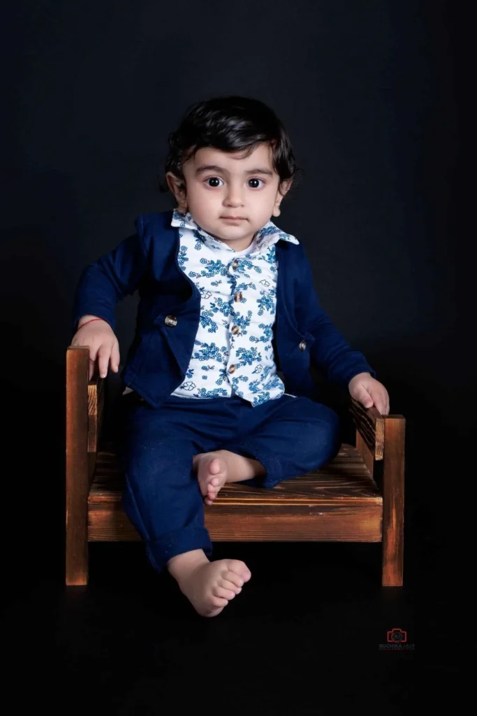 Adorable Kids Portrait: A cute and endearing child sitting on a baby bed, captured with a dark studio background during a Kids Photography session at Ruchika Jain Studio in Wellington, New Zealand