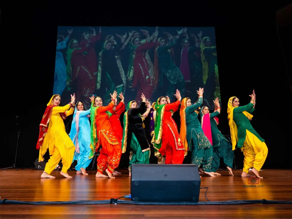 Energetic Punjabi Dance Performance: Traditional Punjabi ladies in colorful shalwar kameez dresses dancing with fervor during a stage show event in Wellington.