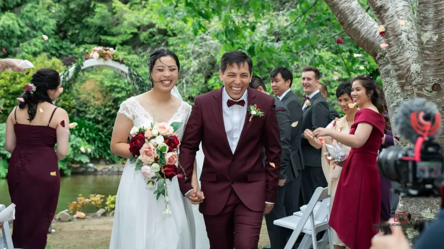 Wellington Wedding Photography: Smiling bride and groom walking hand in hand by the lakeside amidst lush greenery