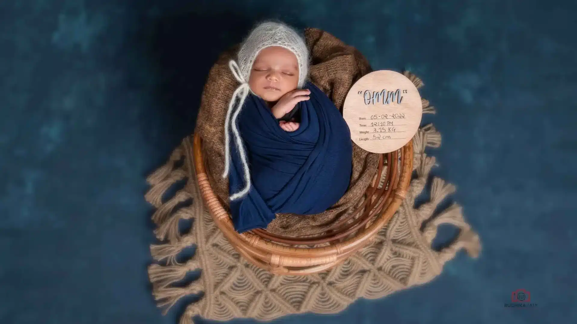 Sleeping newborn wrapped in a blue blanket, resting in a basket with birth details displayed, taken in a Wellington studio