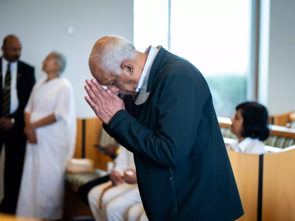 Paying Tribute: An elderly man slightly bent with hands touched, paying his respects at a funeral, captured in a solemn and poignant photograph