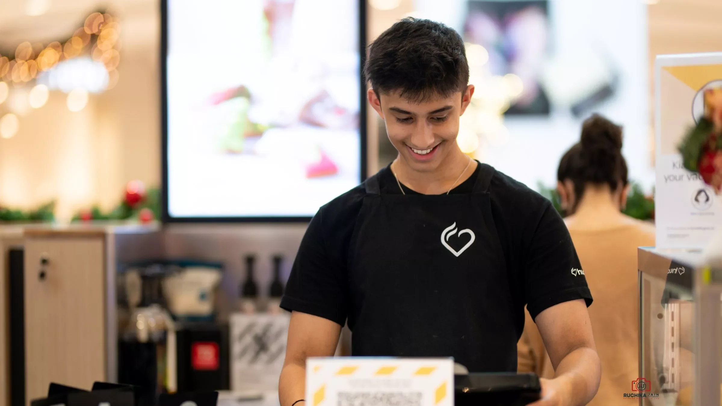 Dedicated Hudsons restaurant worker wearing a black T-shirt with the Hudsons logo, working at the billing counter