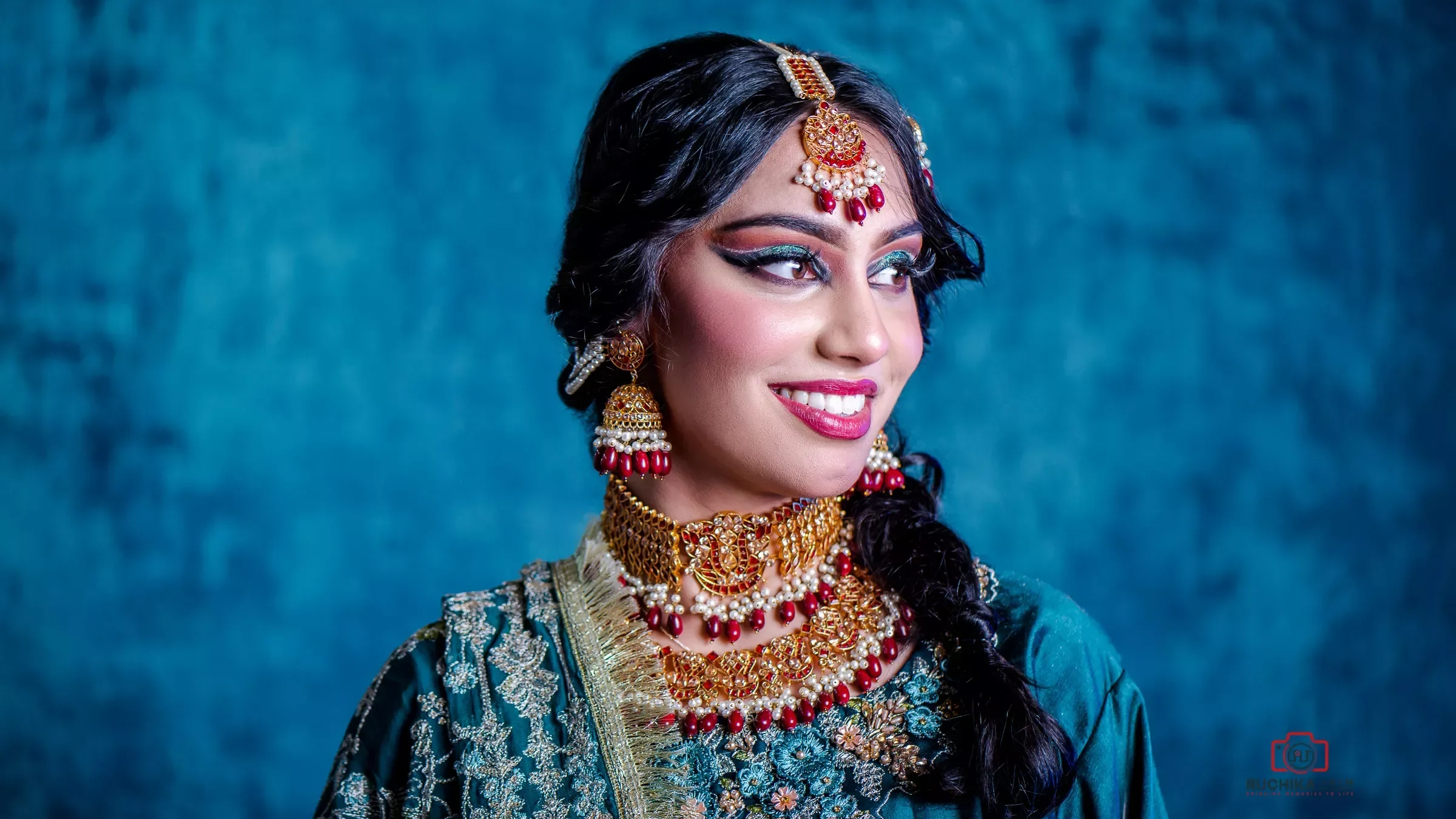 Smiling girl adorned with beautiful jewelry in commercial clothing photography by Ruchika Jain, against a captivating bluish studio background