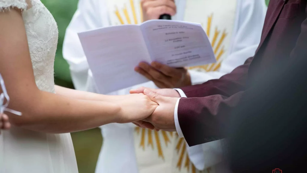 Bride and groom holding hands while celebrant reads - The Ultimate Wedding Guide