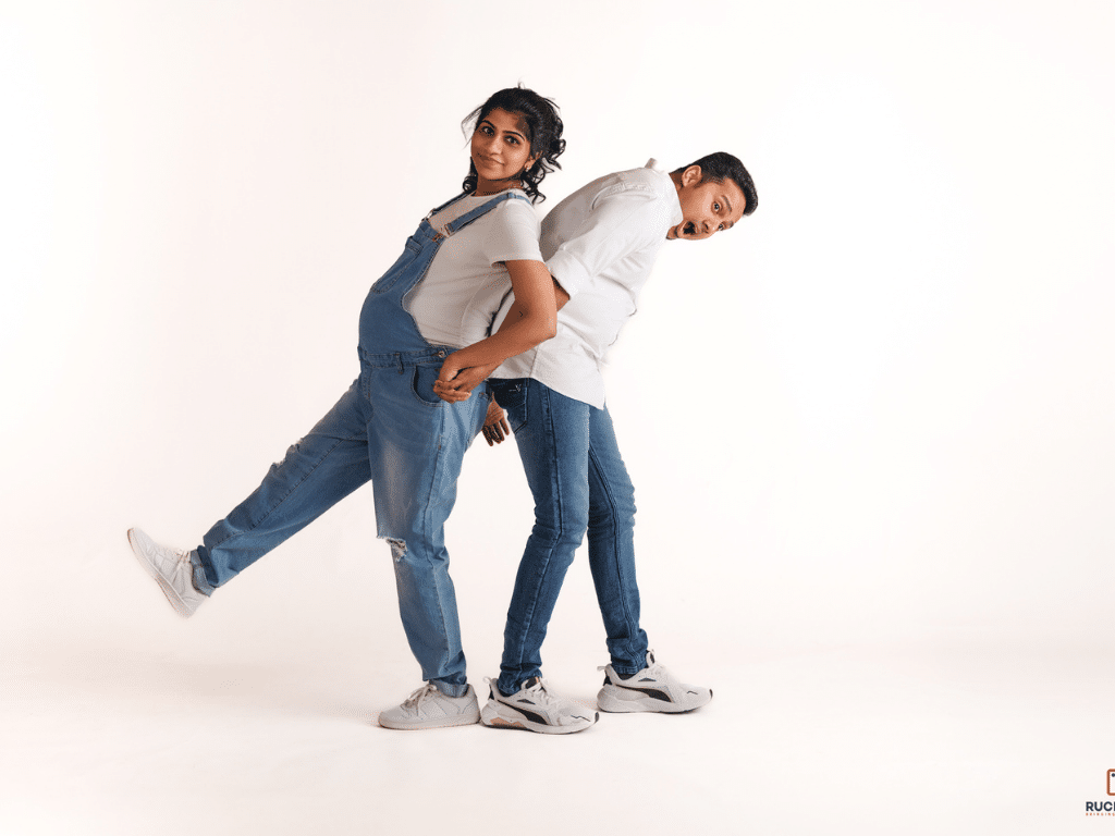 A joyful expecting couple in a playful maternity photoshoot, wearing denim outfits and sharing a lighthearted moment in a professional Wellington studio
