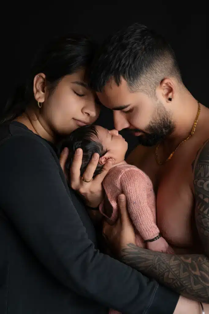 A mother and father lovingly embracing their newborn baby in a warm and intimate setting with a black background